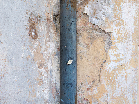 A grey water pipe runs up an old plastered wall that is peeling away.