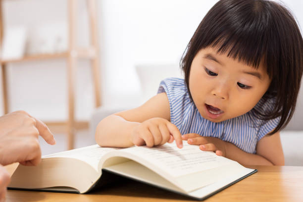 kleines mädchen liest ein buch - child asian ethnicity little girls toddler stock-fotos und bilder
