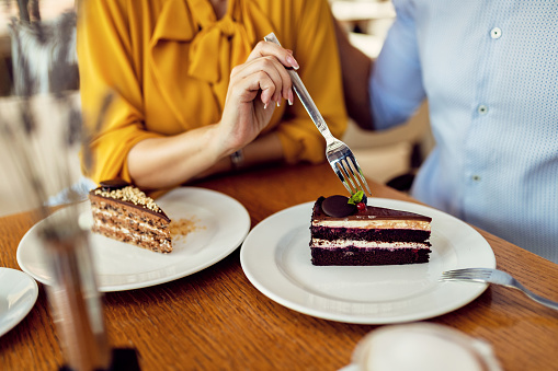 Close-up of unrecognizable couple having dessert and sharing cake in a cafe.