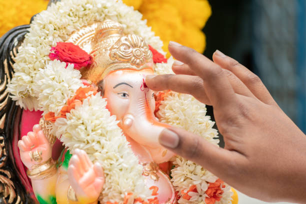 close-up de mãos aplicando tilak ou kumkum ao lorde ganesha durante a cerimônia do festival religioso indiano ganesha ou vinayaka chaturthi. - ganesh festival - fotografias e filmes do acervo