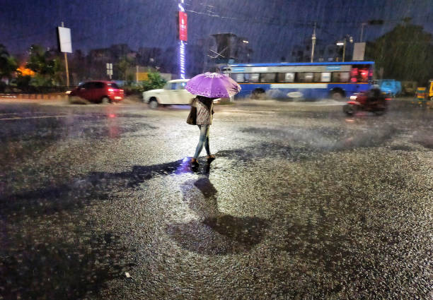 Monsoon In India A woman Crossing a  road during on a heavy rainy night in Kolkata, India. kolkata night stock pictures, royalty-free photos & images