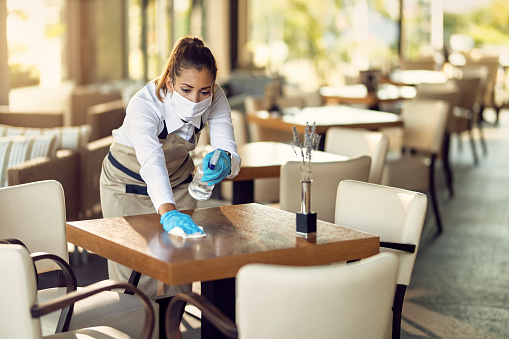 Camarera con mascarilla facial y guantes mesas de limpieza con desinfectante en una cafetería. photo