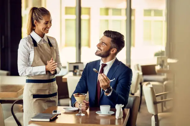 Happy waitress communicating with businessman while serving him dessert in a cafe.