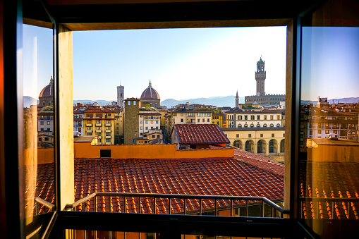 Florence, Italy -- The amazing Florence skyline in the early morning light in a view through a window near Ponte Vecchio. The neighborhood surrounding Ponte Vecchio is undoubtedly one of the most iconic of Florence, with the presence of important noble palaces, Renaissance churches, artisan and goldsmith shops, and some of the most important museums in the world, such as the Uffizi Museum. On the left on the horizon the dome of the Cathedral of Santa Maria del Fiore and on the right the tower and silhouette of Palazzo Vecchio. Image in High Definition format.