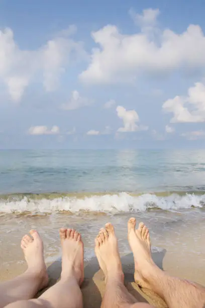 Two people legs on sea beach. Blue sky with clouds