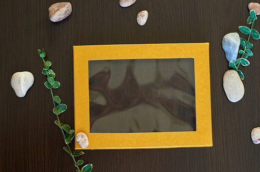 yellow texture frame on a dark brown background. Pebbles and green leaves