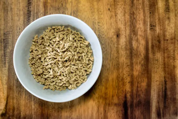 One bowl of dried reconstituted soy protein in a bowl on a wooden table.  This is a textured vegetable protein modern meat substitute used in cooking for vegetarian and vegan meals.  Image taken from directly above.