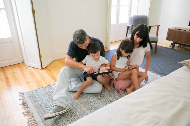 istock Happy family sitting together on floor and using mobile devices 1267093709