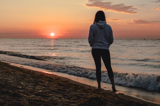 istock woman looking at sunset standing at sea beach 1267094070