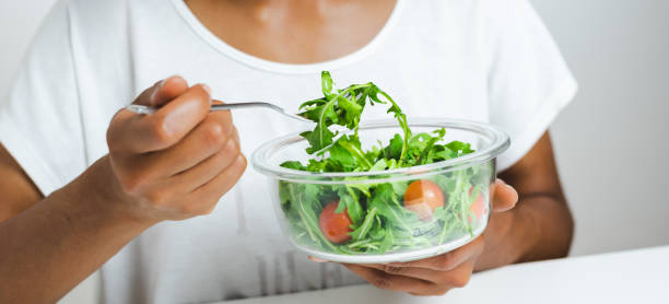 istock lunch box with salad hold by an unrecognizable afro female model. Laptop keyboard reflected on glass. 1267097760
