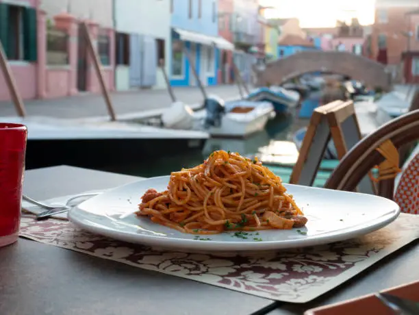 Photo of Plate of Italian spaghetti with seafood on a restaurant table in Burano, the town of colorful houses in Venice, Italy