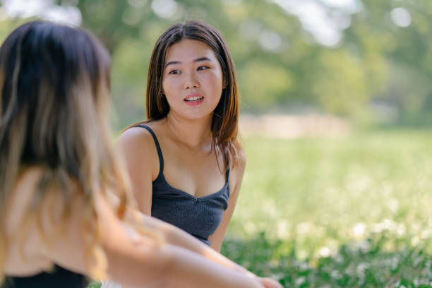 Two female friends are enjoying talking with each other while sitting and resting in outdoors in a public park.