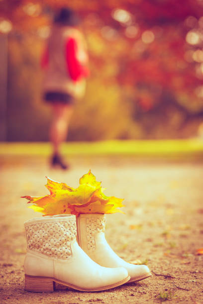 Autumn nature outdoors concept. Leaves in white boots n the park. Woman walking in the background.