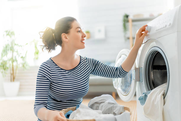 woman is doing laundry Beautiful young woman is smiling while doing laundry at home. washing machine photos stock pictures, royalty-free photos & images