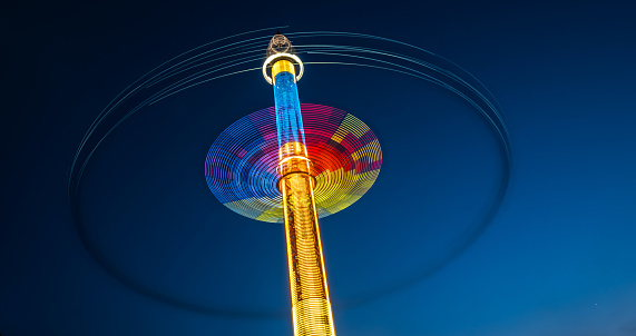 Abstract blurred multicolour spinning high speed carousel in front of dark night sky in amusement park