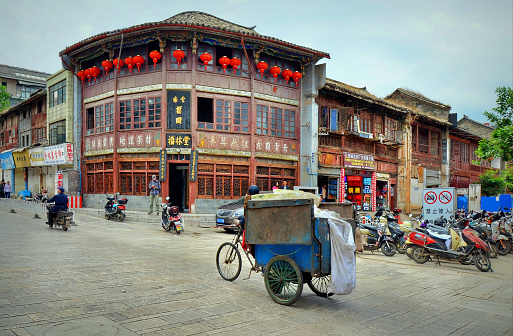 Street life in Kunming city, Yunnan province, China. Tricyle and motorbikes on a road at an old quarter with traditional wooden buildings.