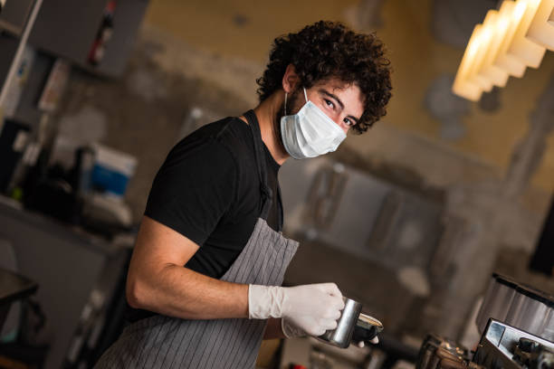 jonge mens, barista, die koffie espresso maakt terwijl het dragen van chirurgisch masker en handschoenen voor het verhinderen van coronavirusverspreiding. - andrej stockfoto's en -beelden
