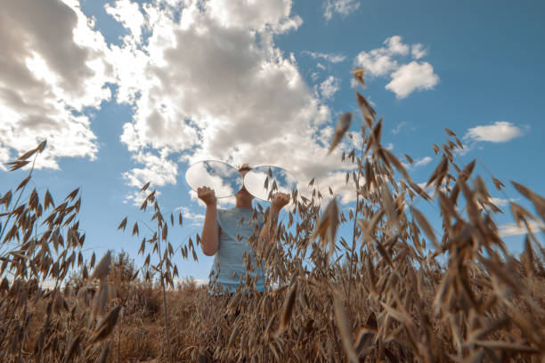 istock A boy with two round mirrors, in which the sky is reflected in glasses, stands in a field of wheat 1267123016