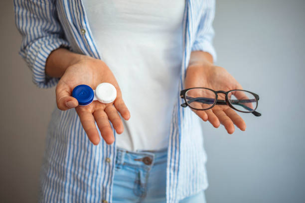 Young woman choosing between contact lenses or glasses Young woman holding contact lens case and glasses on blurred background. Woman hold contact lenses and glasses in hands close up. concept of choice of vision protection contact lens photos stock pictures, royalty-free photos & images