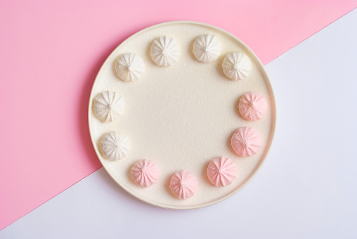 Pink and white plate with meringue sweet dessert cookies flat lay top view. Sweet beautiful candy colors abstract