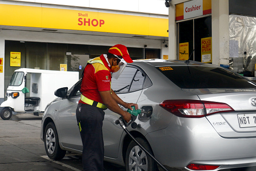 Antipolo City, Philippines - August 10, 2020: Gasoline station employee serves a customer and refills the gas tank a vehicle.