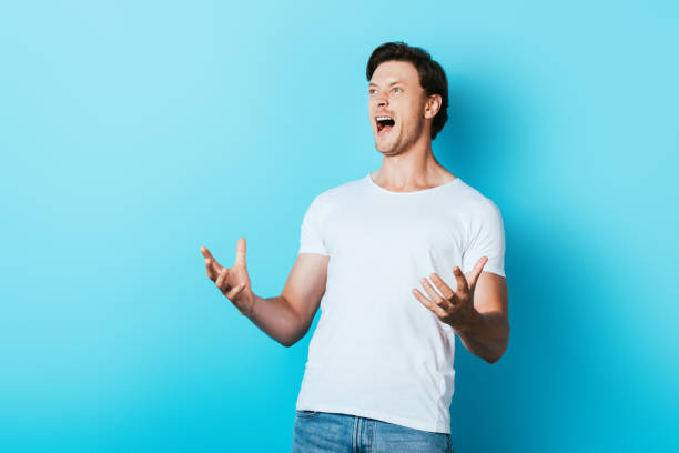 istock Angry man in white t-shirt screaming on blue background 1267132120