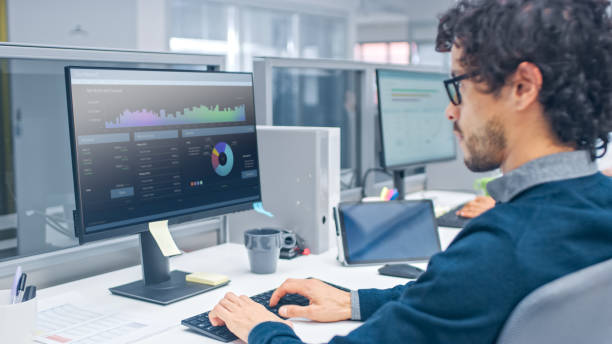 istock Young Handsome Manager with Curly Hair Works on a Desktop Computer in Accountant Software. Diverse and Motivated Business People Work on Computers in Modern Open Office. 1267134369