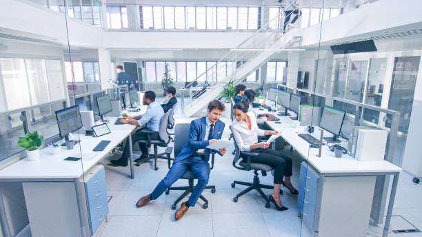 istock Diverse Multinational Team of Business Managers and Specialists Work on Desktop Computers, Young Businessman Asks Question to Female Colleague. Young and Motivated Business People in Modern Office. 1267134377