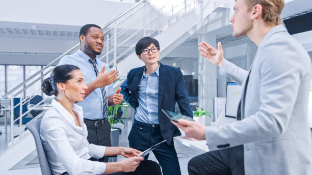 istock Diverse Multinational Team of Business Managers and Specialists Chat and Discuss Graphs on Paper and Tablet Computer. Young and Motivated Business People in Modern Open Office. 1267134427