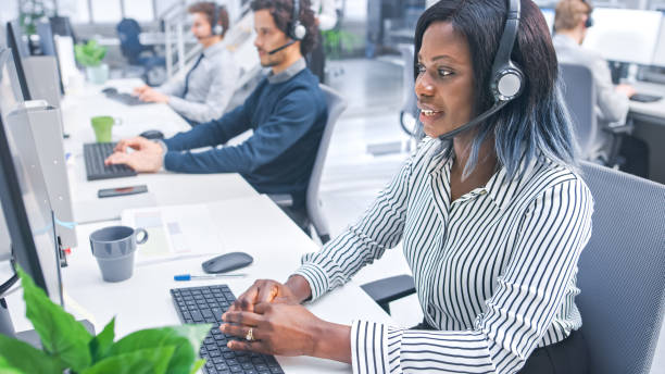istock Beautiful Young Female Customer Service Operator Working in a Busy Modern Call Center with Diverse Multicultural Team of Office Specialists Wearing Headsets and Taking Calls. 1267134566