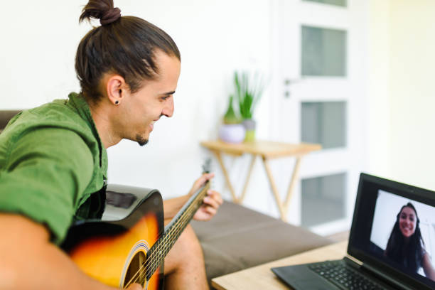 istock Young caucasian man playing the guitar in front of the computer during an online conversation.  / Online music lesson concept. 1267135600