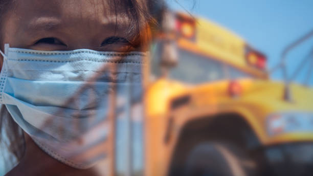 Composite image of female student with concerned look wearing face mask in front of blurred image of school bus stock photo