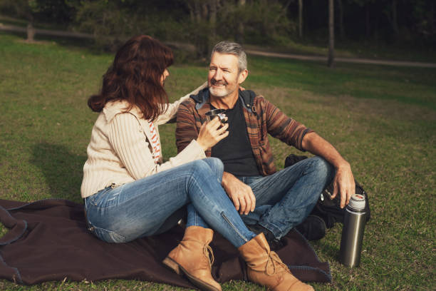 istock Middle-aged couple sitting on the grass in park, hugging and drinking tea. 1267141529
