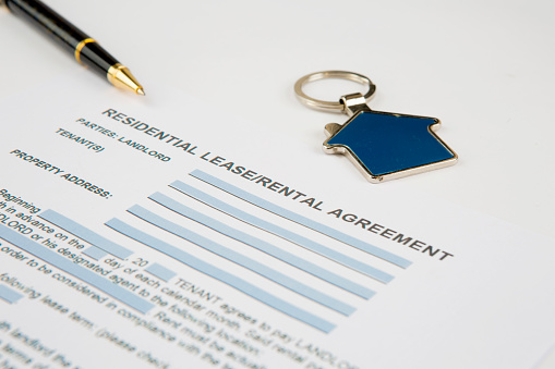 Lease agreement document with house keyring and pen. Residential lease, rental agreement. Real estate concept. Horizontal close-up.