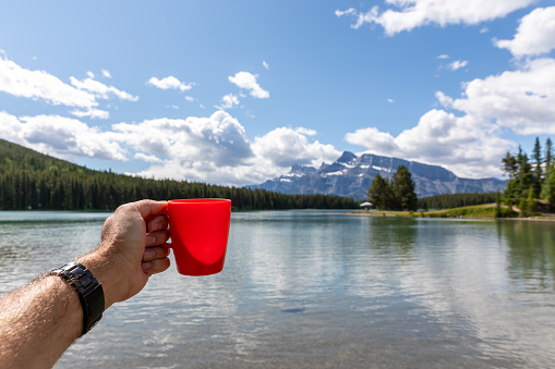 Human Hand Showing a coffee cup at Lake Minnewanka, Banff, Canada
