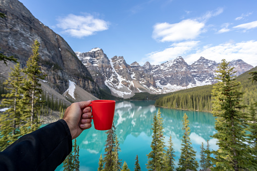 Human Hand Showing a coffee cup at Moraine Lake in Banff National Park, Canada