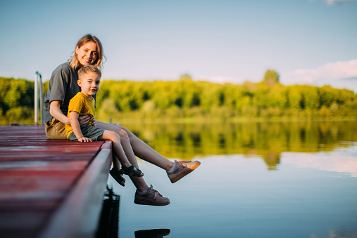 Cool kid boy with mother sitting on dock. Summer photography for a blog or advertising about family and travel. High quality photo