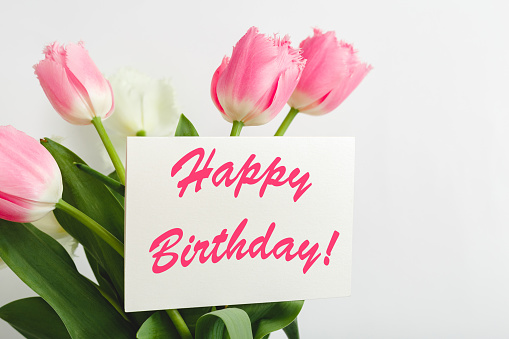 Happy Birthday text on gift card in flower bouquet. Beautiful bouquet of fresh flowers tulips with greeting card Happy Birthday on white background