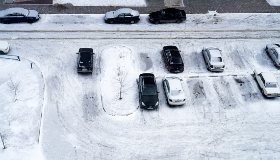 Top view of snow-covered parked cars in the courtyard of a multi-storey residential building in winter.