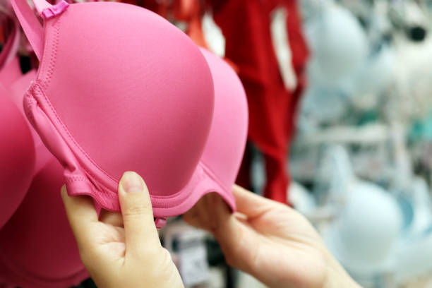 Woman chooses pink support bra hanging on rack in lingerie store stock photo