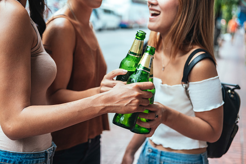 Group of female hands holding green beer bottles making toast outside