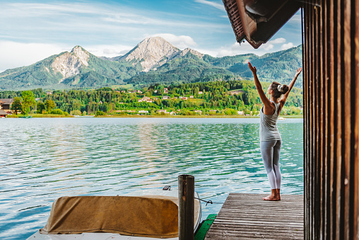 Reconnection to Nature – Outdoor Meditation and Yoga during sunrise on a jetty at Lake Faak, Austria, looking at mountain Mittagskogel/Kepa, the third highest mountain of the Karawanks mountain range