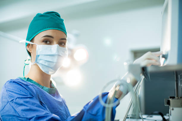 Female doctor preparing an anesthesia machine in an operating room Portrait of a young female doctor in scrubs and a protective face mask preparing an anesthesia machine before an operation anaesthetist stock pictures, royalty-free photos & images