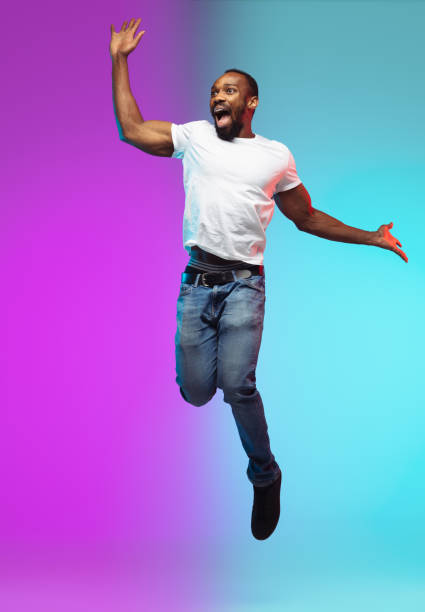 afro-amerykański portret młodego człowieka na gradientowym tle studia w neon, skacząc wysoko - flying contemporary dancing dancer zdjęcia i obrazy z banku zdjęć