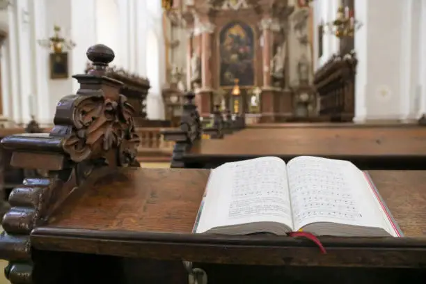 Photo of Bible or prayer book lying on praying bench in catholic church, selective focus