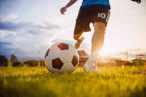 地域の農村部で運動のためのストリートサッカーサッカーを楽しんでいる子供のグループの屋外シルエットアクションスポーツ。開発国の貧しい子どもたちと貧困の子どもたち。 - 子供サッカー ストックフォトと画像
