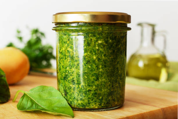 Homemade pesto sauce in a glass jar with basil, ingredients and baguette on white table in the kitchen. Pesto - traditional italian sauce for fettuccine, focaccia, pizza, toast, sandwiches. Homemade pesto sauce in a glass jar with basil, ingredients and baguette on white table in the kitchen. Pesto - traditional italian sauce for fettuccine, focaccia, pizza, toast, sandwiches pesto sauce stock pictures, royalty-free photos & images