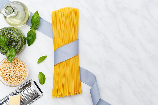 Raw spaghetti tied with a ribbon with mock up.Pesto sauce with ingredients on white marble table.Making Spaghetti,pesto sauce tradition Italian recipe.Top view,frame,flat lay with copy space for text