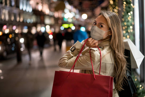 Happy woman Christmas shopping wearing a facemask Happy woman Christmas shopping and wearing a facemask while carrying bags â COVID-19 pandemic concepts shopping bag photos stock pictures, royalty-free photos & images