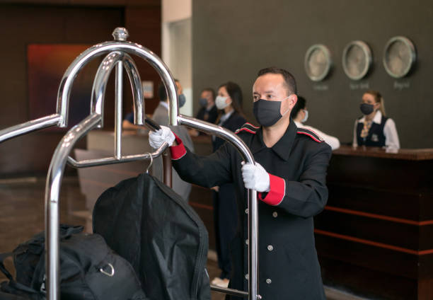 Bellboy working at a hotel wearing a facemask Friendly bellboy working at a hotel wearing a facemask while carrying luggage on a cart - COVID-19 concepts bellhop stock pictures, royalty-free photos & images